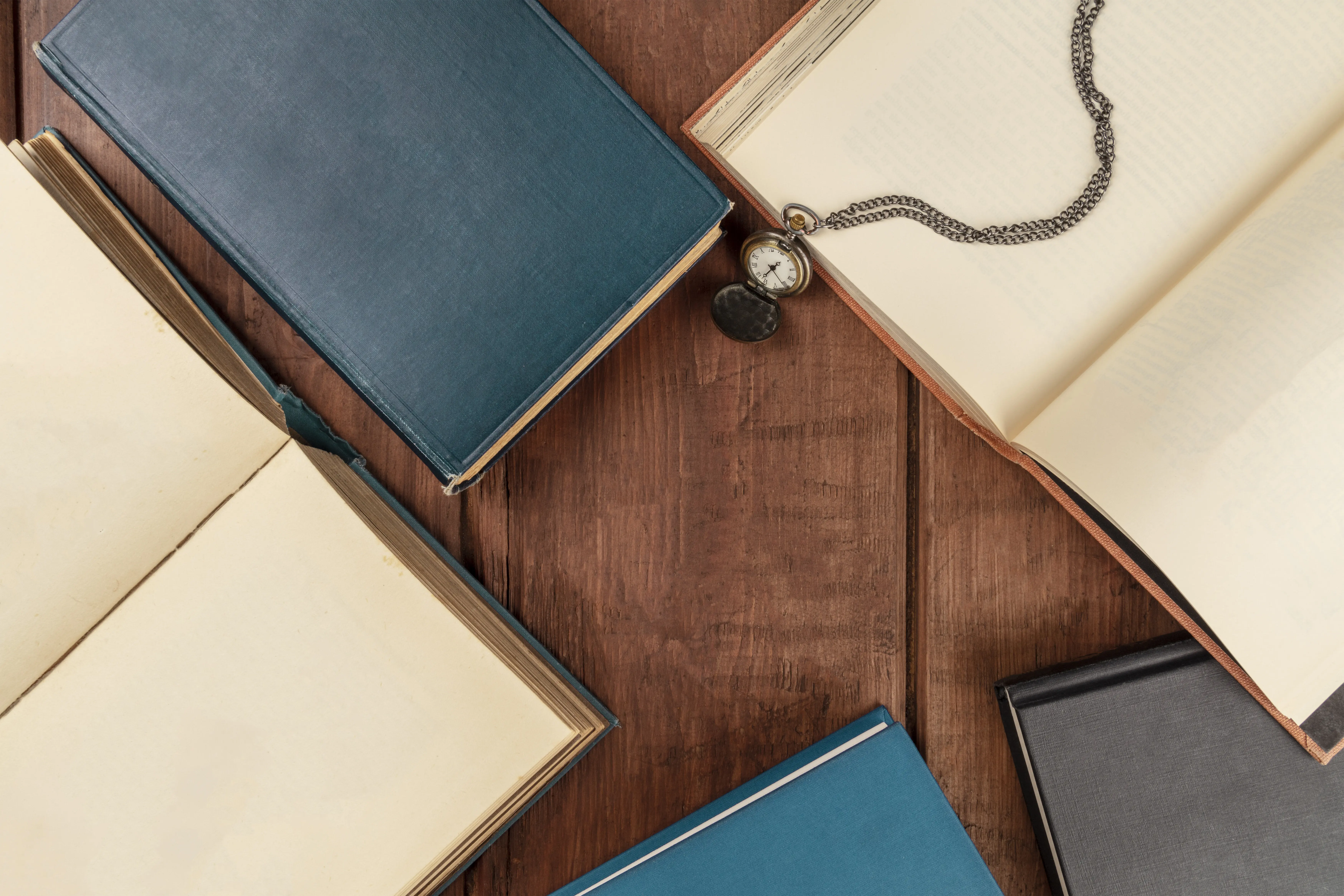 Foto in Draufsicht von Büchern auf dunklem Hintergrund mit einer Vintage-Uhr und Freiraum für Text.